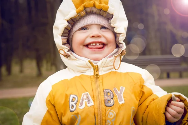 Bambino sorridente in natura in abiti caldi all'inizio della primavera. Bambino allegro in cappuccio all'aperto. Ritratto di bambino con sorriso felice . — Foto Stock