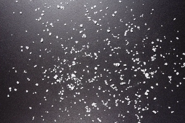 La sal marina está esparcida sobre fondo negro. Fondo negro texturizado con granos de sal . — Foto de Stock