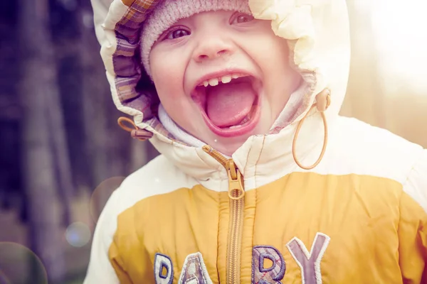 Портрет маленького счастливого ребенка в капюшоне и теплая одежда ранней весной. Смеющийся ребенок в природе — стоковое фото