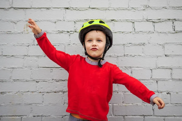 Anak-anak bermain helm di dinding bata putih. anak itu merentangkan tangannya dan dengan senang hati mempersembahkan dirinya sebagai pesawat terbang . — Stok Foto