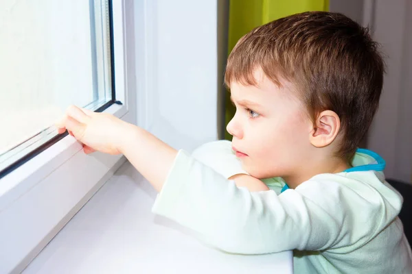 Anak kecil yang sedih melihat ke luar jendela. Potret anak Kaukasia dekat jendela. Anak Melankolis . — Stok Foto