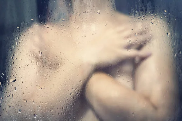 Menina nua no chuveiro atrás de um copo molhado com gotas de água . — Fotografia de Stock