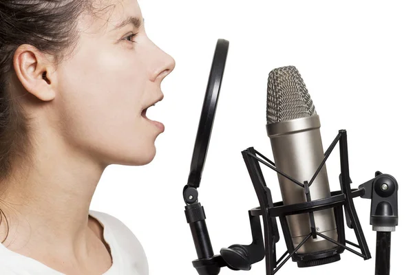 Brunette meisje records stem naar studio microfoon. Jonge vrouw zingt in de studio condensatormicrofoon met spider geïsoleerd op een witte achtergrond. Schrijven lied in correcte opnamestudio. — Stockfoto