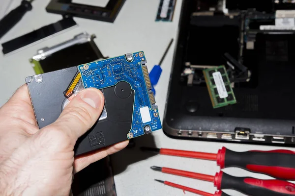 Technical service of laptops. Parts of computer. Hard drive from laptop in the hand of computer repair specialist on the background of disassembled notebook