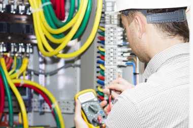 mühendis ölçümleri multimetre ile elektrik dolapta yapar. Elektrikçi elektrik paneli arka plan üzerinde elinde Sınayıcısı ile. Elektrik sigorta kutusu düzeltilmesi