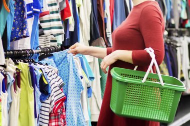 Kız alışveriş sepeti ile giysi süpermarkette seçer. Süpermarket kavramında kıyafet satın. Mega alışveriş merkezinde alışveriş