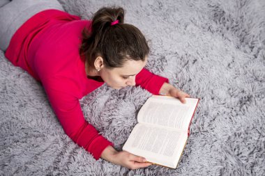 Güzel esmer genç kadın rahat daire yatakta kitap okuyor. Hobi kitap okumak ve kurgu. Kitap ile vakit geçirmek. Bir kız evde kurgu okur.
