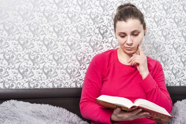 Attraente giovane donna carina che legge un romanzo a casa. Una ragazza sta leggendo un libro. Un hobby letterario. Lettura di finzione. Trascorrere del tempo con il libro — Foto Stock