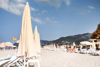 Tropikal resort kumlu plaj yumuşak seçici odak. Plaj şemsiyeleri ve şezlong veya şezlong parlak açık gün. Deniz plaj yaz tatili. Dağlar kumsalına yakın.