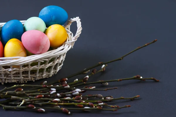 Easter background. Easter multicolored eggs in a basket and a willow branch on a black background. Religious Christian Easter holiday concept.
