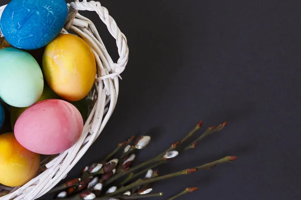 Easter background. A view of Easter colorful colored eggs in basket and a willow branch on black background. Religious Christian holiday concept. Preparation for Easter.