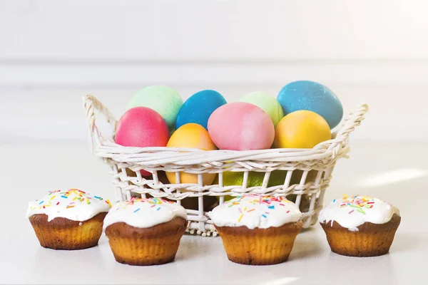 Holiday Easter concept. Multicolored easter eggs in a basket, sweet cupcakes. Easter background. Treats for the spring religious Christian holiday