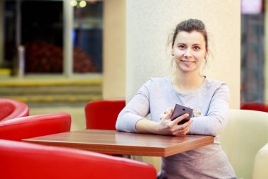 Genç çekici kız elinde smartphone ile kafe alışveriş merkezinde masada oturuyor. Şirin kadınla telefon elinde Restoran kafede masada.