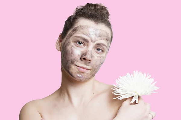 Jonge vrouw met zwart masker geïsoleerd op roze achtergrond. Huid zorg concept. Aantrekkelijk meisje met witte bloem. Spa-behandelingen. Reinigen huid gezicht — Stockfoto