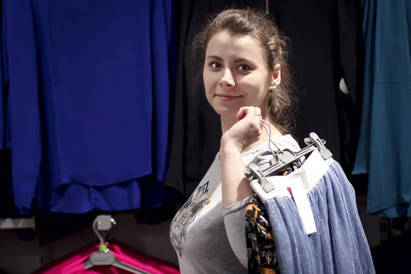 Young girl buys clothes in fashionable boutique shop. Shopping concept. The girl in the clothing store is holding things on the hangers. Buying new clothes. — Stock Photo, Image