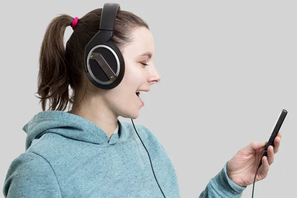 Young attractive brunette girl in headphones with player. Beautiful woman listening to music with headphones isolated on gray background. Girl in sweatshirt with headphones and player in hands. — Stock Photo, Image