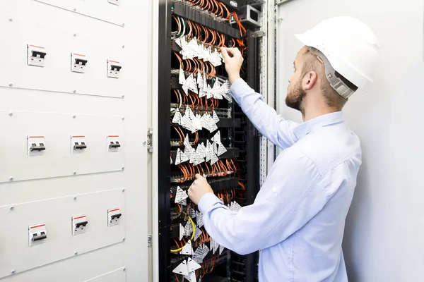 Engenheiro de serviço no data center. Trabalhador em um capacete perto dos interruptores de cabos ópticos. Engenheiro de telecomunicações no data center. Instalação de equipamentos de rede de computadores e armazéns de dados . — Fotografia de Stock