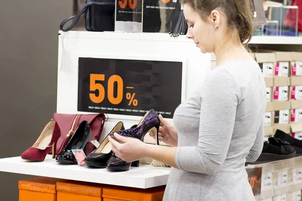 Brunette girl in store is choosing shoes. woman in fashion boutique buys shoes. Shopping in the shopping center. girl is holding fashionable shoes with heels. Sale in the shoe store.