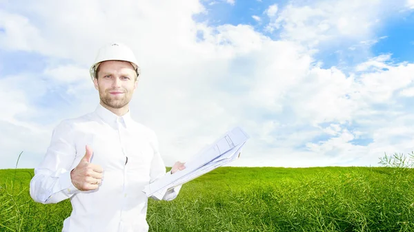 Geoloog in wit helm op groene weide met tekeningen in handen houdt zijn duim omhoog. Ingenieur bouwer op bouwplaats — Stockfoto