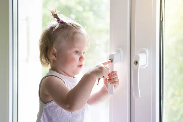 Dítě otevře okno s zámkem. Ochrana proti vypadnutí dítěte z okna. malá holčička stojí na parapetu. dítě si hraje s klíče v okně. — Stock fotografie