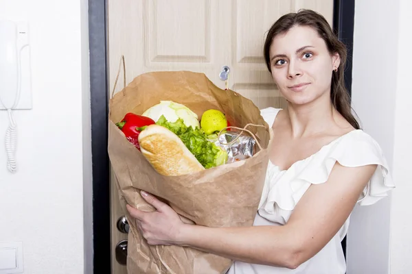 girl came home with package of food. young woman brought home from grocery store vegetables. Purchase of products. concept of a healthy diet. Housewife with  products on background of door of house.
