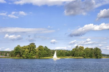 Parlak güneşli yaz gününde beyaz yat ile göl manzara. Beyaz bulutların üzerinde Trakai ve yeşil ağaçlar ve ufuk tepelerinde büyük göller ile mavi gökyüzü. Tekne ya da göl kenarında gemi.