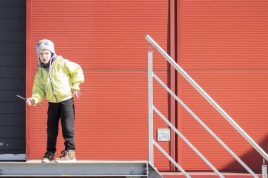 Çocuk robot gibi hareket eder. Çocuk çerçevede metal profil duvar endüstriyel tesis topraklarının çalış. Şapkalı çocuk ve sanayi bölgesi ceketle portre.