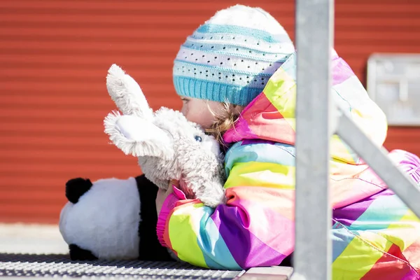 Маленька дівчинка обіймає плюшеві іграшки, граючи на міському подвір'ї . — стокове фото