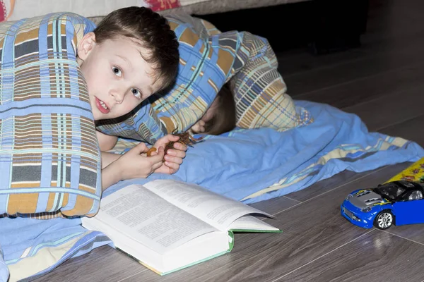 Маленькие дети читают книгу под одеялом. Мальчик играет под одеялом в доме перед сном . — стоковое фото