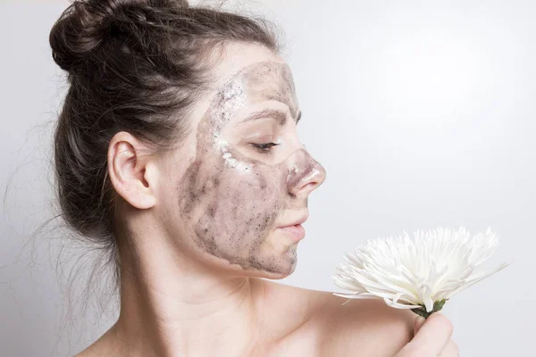 Aantrekkelijke brunette meisje met witte bloem in gezichtsmasker. Reiniging en bescherming van de huid van gezicht. Huidverzorging. Portret van een meisje met zwarte cosmetische masker. — Stockfoto