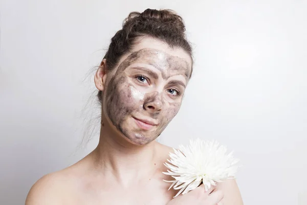 Portret van aantrekkelijke brunette meisje met zwarte cosmetische gezichtsmasker en ruimen witte bloem. Zorg van de huid van het gezicht masker. Spa-behandelingen. — Stockfoto