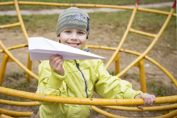 在操场上的白人小男孩的肖像与纸飞机在手。孩子们在户外玩纸飞机. — 图库照片