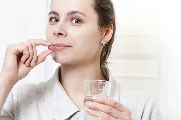 Белая брюнетка принимает таблетки и пьет стакан чистой воды. Девушка держит в руках лекарство и стакан воды. концепция здоровья, терапевтическая терапия. Лекарства . — стоковое фото
