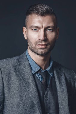 Arka plan gri duvar üzerinde moda saç kesimi ile gri elbiseli şık başarılı acımasız adam portresi. Kıl brunet genç adamla güzel.