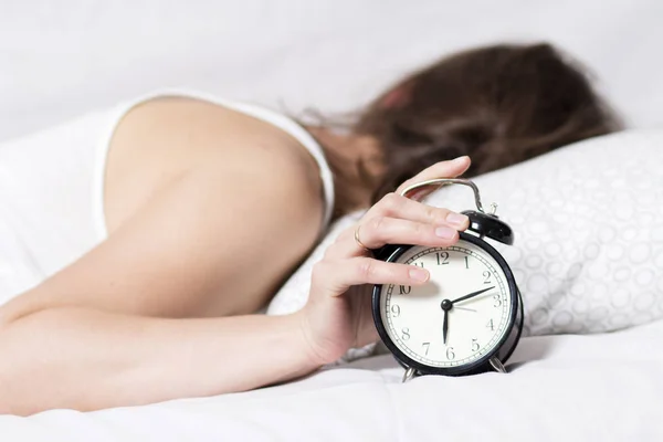 Ragazza sta dormendo sul letto in camera da letto e spegne sveglia. donna non vuole svegliarsi presto al mattino. La ragazza si e 'allontanata dalla sveglia. Alzati presto per lavorare. Sonno femminile . — Foto Stock