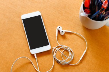 Ahşap arka planda boş ekranlı ve kulaklıklı akıllı telefon