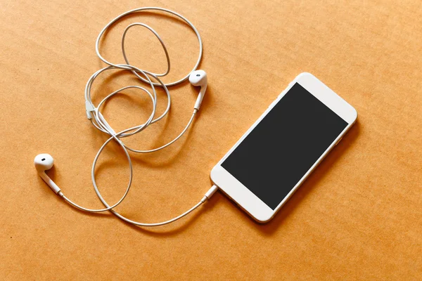Pusty biały smartfon i słuchawki na drewnianym tle — Zdjęcie stockowe