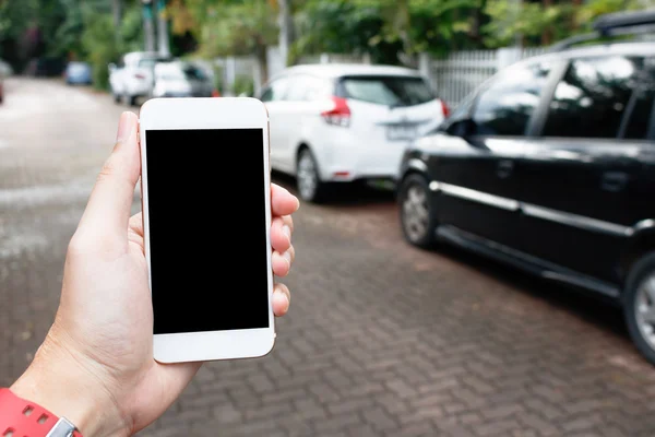 Hombre de mano sosteniendo el teléfono inteligente que muestra la pantalla en blanco con los coches borrosos — Foto de Stock