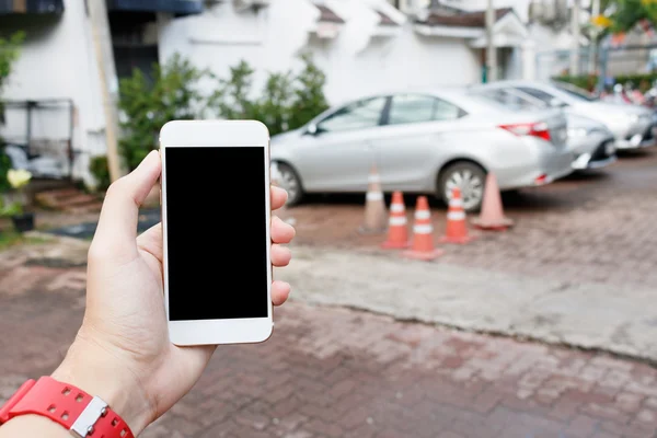 Hombre de mano sosteniendo el teléfono inteligente que muestra la pantalla en blanco con los coches borrosos — Foto de Stock