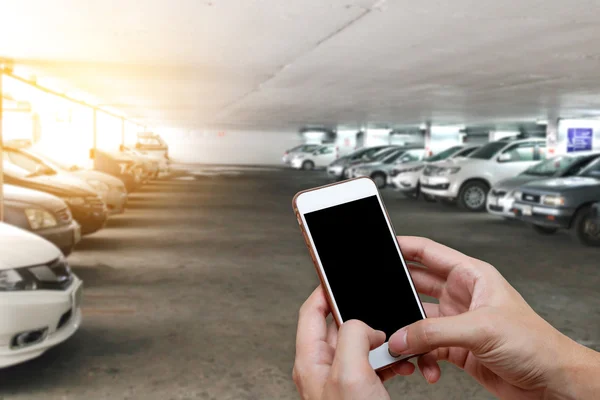 Telefone inteligente mostrando tela em branco na mão do homem com carros embaçados estacionamento — Fotografia de Stock