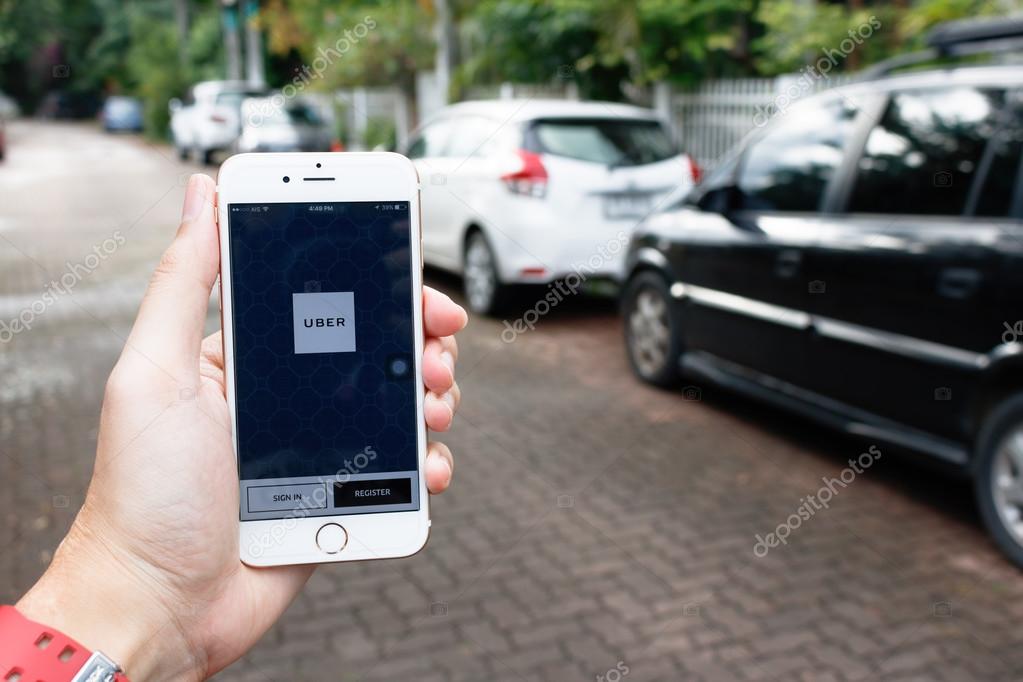 CHIANG MAI,THAILAND-SEP 02,2016 :A woman hand holding Uber application startup page on the Apple iPhone 6 display in female hand. Blurred street view with car,Uber is app-based transportation network.