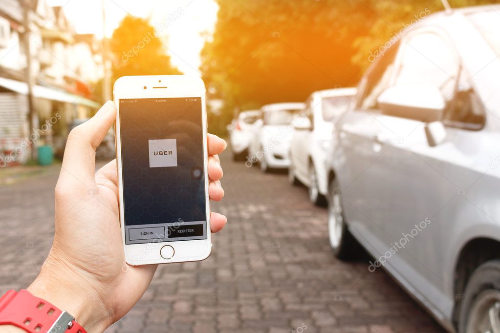 CHIANG MAI,THAILAND - SEP 02,2016 : A woman hand holding Uber application startup page on the Apple iPhone 6 display in female hand. Blurred street view with car,Uber is smartphone app-based transportation network.