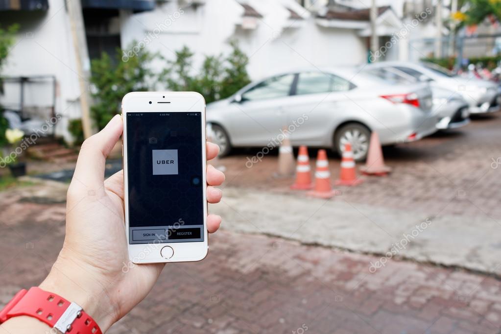 CHIANG MAI,THAILAND-SEP 02,2016 :A woman hand holding Uber application startup page on the Apple iPhone 6 display in female hand. Blurred street view with car,Uber is app-based transportation network.