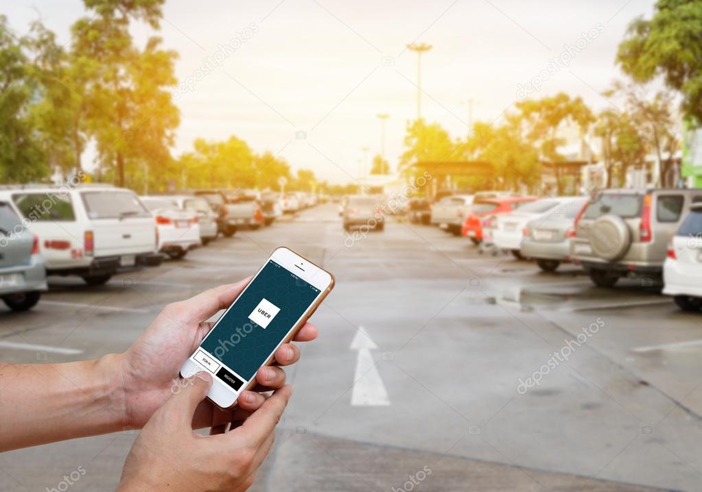CHIANG MAI,THAILAND-JUNE 25,2016 :Man hand holding Uber application startup page on the Apple iPhone 6 display in male hand. Blurred street view with car, Uber is app-based transportation network.
