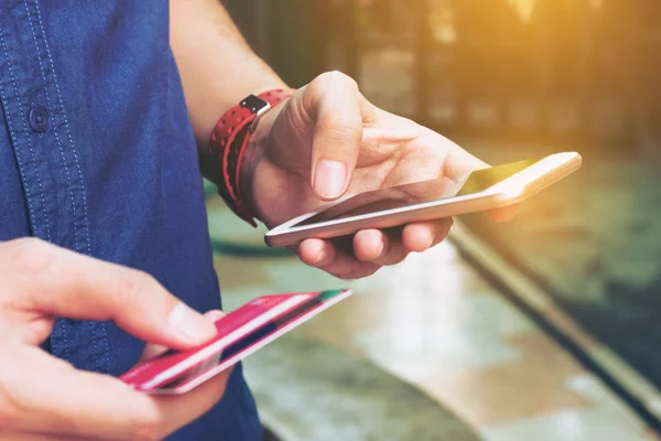 Hombre utilizar el teléfono inteligente y la celebración de la tarjeta de crédito con compras en línea — Foto de Stock