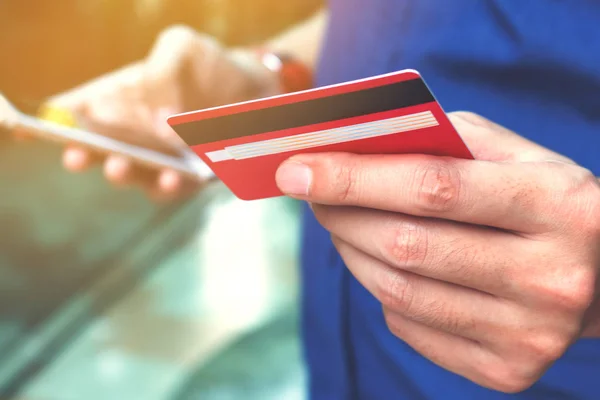 Kredi kartı tutan ve akıllı telefon kullanan genç adam yakın çekim 