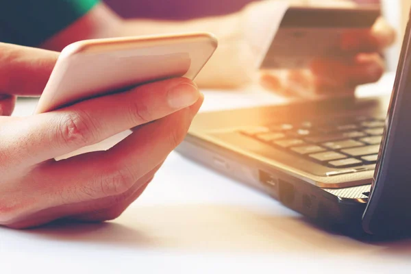 Joven usando teléfono inteligente y la celebración de la tarjeta de crédito con el ordenador portátil f —  Fotos de Stock