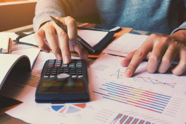 Hesap makinesini kullanarak ve kağıt grafik masa üzerine işaret eden işadamı.