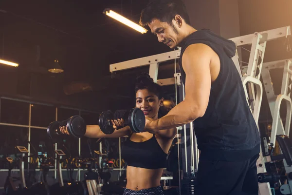 Pessoal de treinamento homem ajudando os braços das mulheres para puxar para cima haltere f — Fotografia de Stock