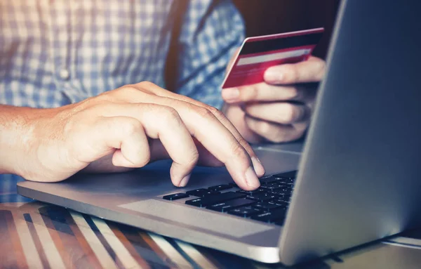 La mano del hombre escribiendo en el ordenador portátil del teclado y la celebración de la tarjeta de débito para — Foto de Stock